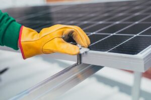 Close-up of a worker's hand with protective gloves adjusting a bolt on a solar panel.