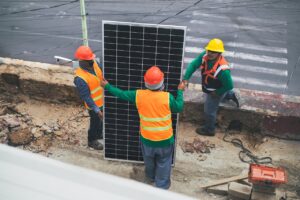 Workers wearing PPE install solar panels for sustainable energy at a construction site.