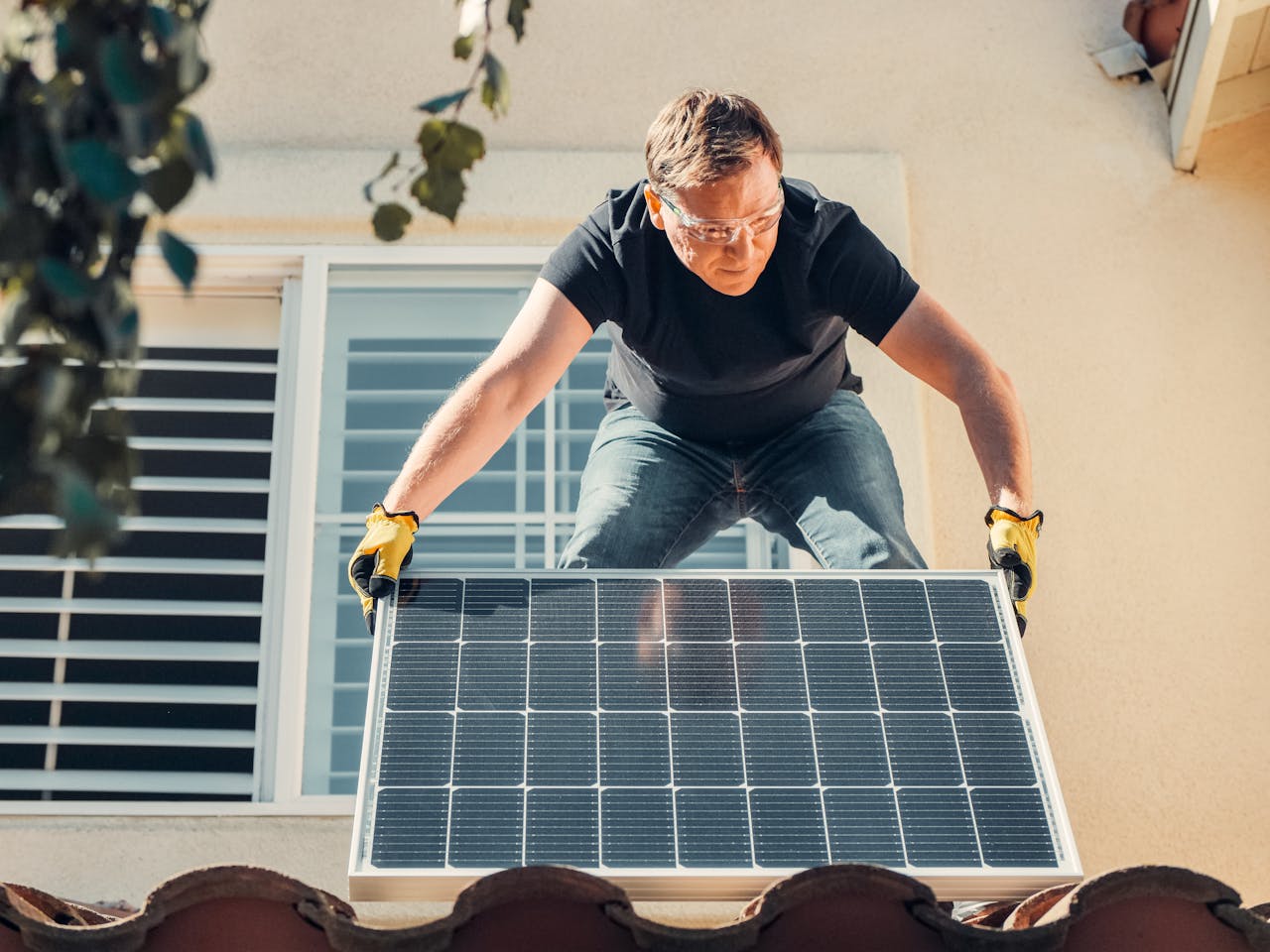 A man in safety glasses installs a solar panel on a house roof, promoting renewable energy.